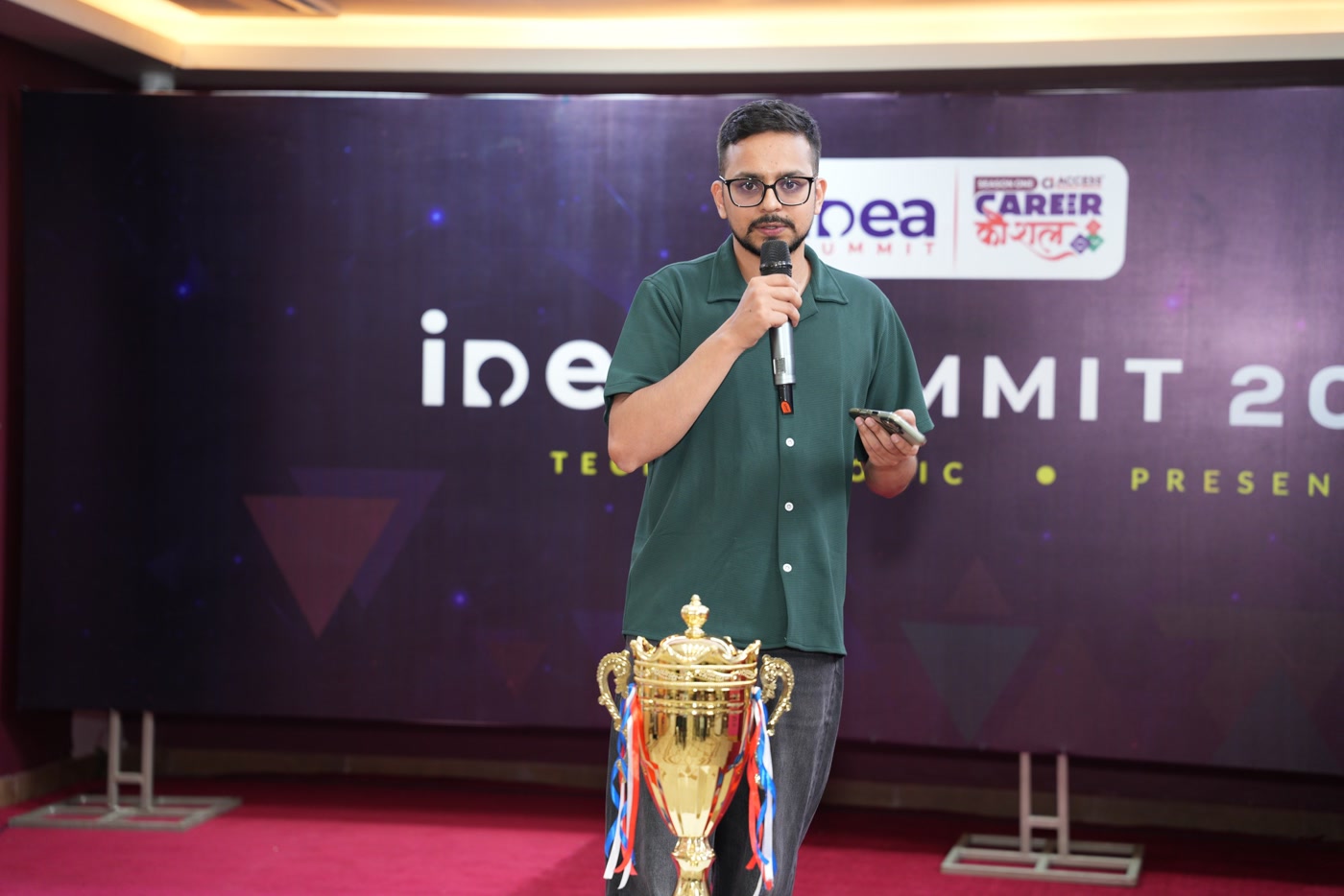 Laxman speaking at Idea Summit 2026, with the event logos and trophy visible